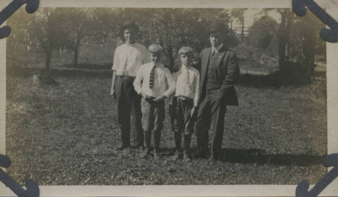 Untitled [Two men stand with two children on field]