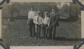 Untitled [Two men stand with two children on field]