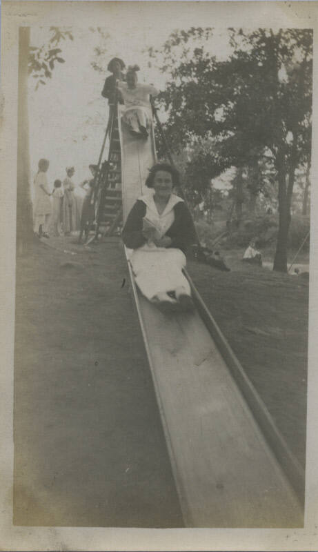 Untitled [Woman goes down slide, children in background]