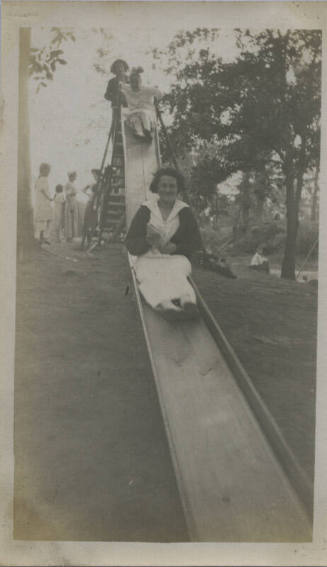 Untitled [Woman goes down slide, children in background]