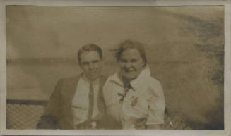 Untitled [Woman and man sit together, body of water in background]
