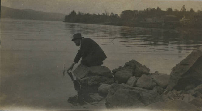 Untitled [Man kneels by water and dips hand in it]