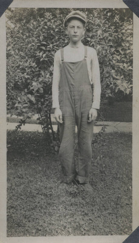 Untitled [Man stands in front of tree, wears overalls]