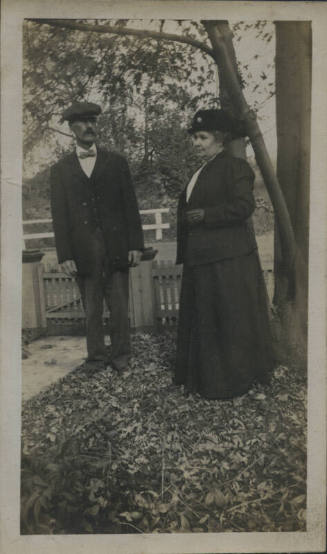 Untitled [Woman and man stand on lawn, leaves on ground]