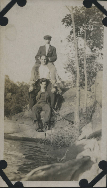 Untitled [Three men sit and stand on rocks]