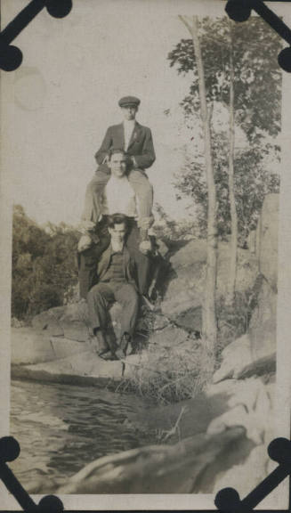 Untitled [Three men sit and stand on rocks]