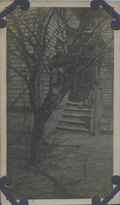 Untitled [Man sits on tree, house in background]