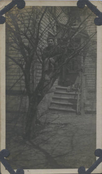 Untitled [Man sits on tree, house in background]