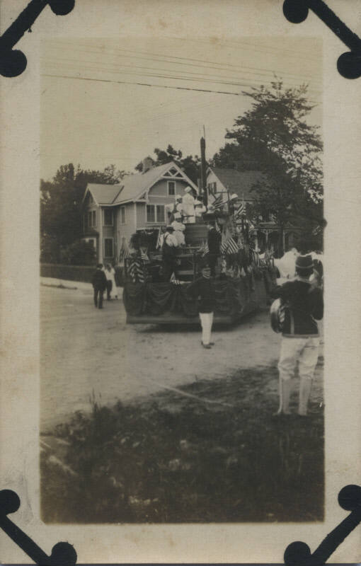 Untitled [Crowd stands on stree and parade cart, decorated in American flags]