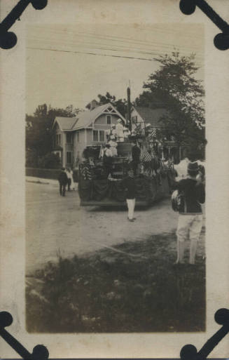 Untitled [Crowd stands on stree and parade cart, decorated in American flags]