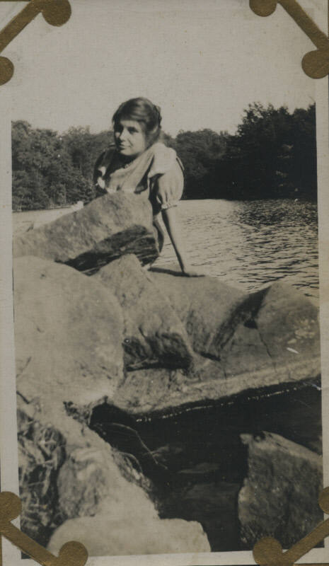 Untitled [Woman sits on rocks, body of water in background]