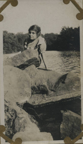 Untitled [Woman sits on rocks, body of water in background]