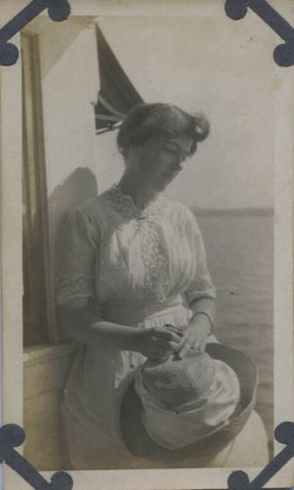 Untitled [Woman stands, holds hat in hands, looks down]