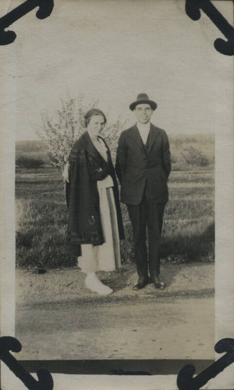 Untitled [Woman and man stand on road, field in background]