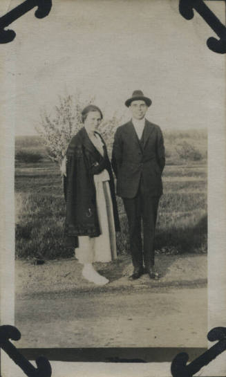 Untitled [Woman and man stand on road, field in background]