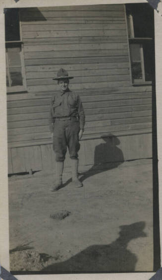 Untitled [Man in uniform stands, building in background]