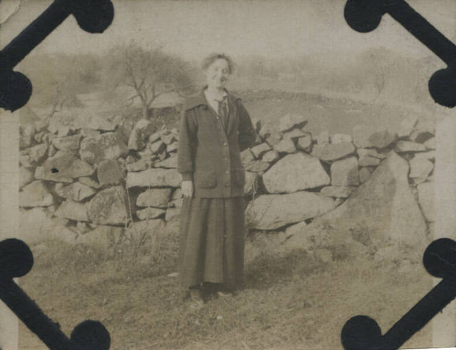 Untitled [Woman stands in front of rock fence]