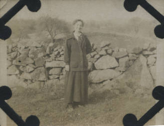 Untitled [Woman stands in front of rock fence]