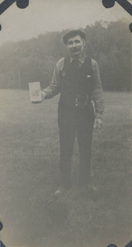 Untitled [Man stands on field, holds up book]