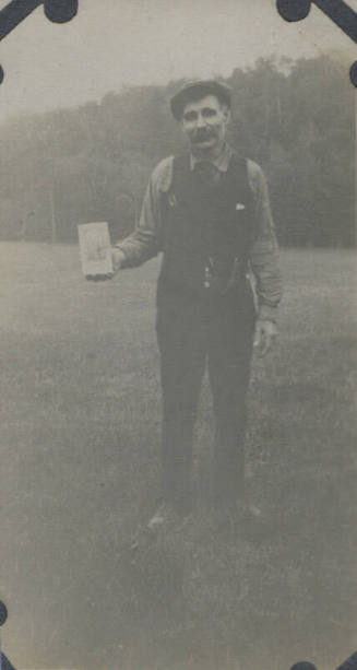 Untitled [Man stands on field, holds up book]