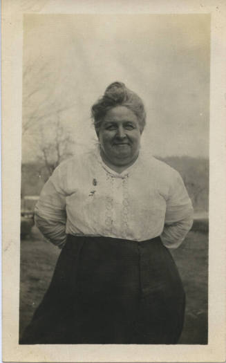 Untitled [Woman stands on field, hands behind back]