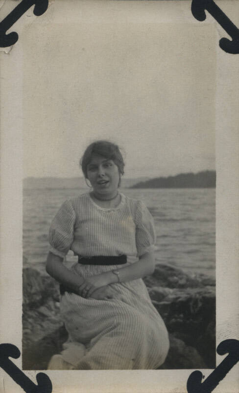 Untitled [Woman sits on rocks, body of water in the background]