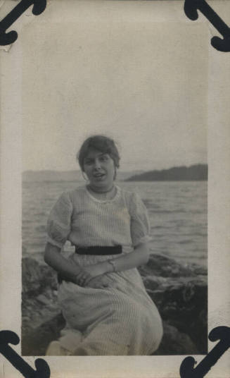Untitled [Woman sits on rocks, body of water in the background]