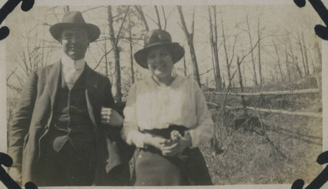 Untitled [Woman and man stand in woods, fence by their side]