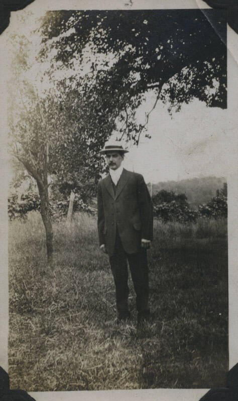 Untitled [Man stands on field, wears hat]