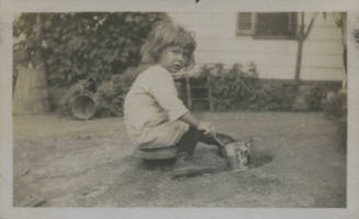 Untitled [Child sits on lawn, plays with bucket]