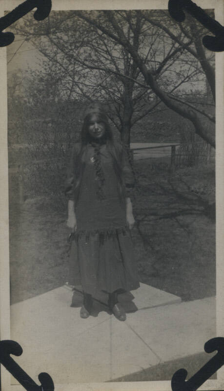 Untitled [Woman stands, arms by her sides, trees in background]