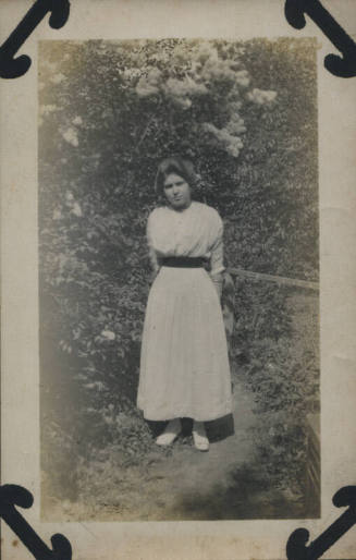 Untitled [Woman stands in garden, arms behind back]