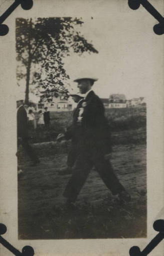 Untitled [Men walking on dirt road, houses in background]