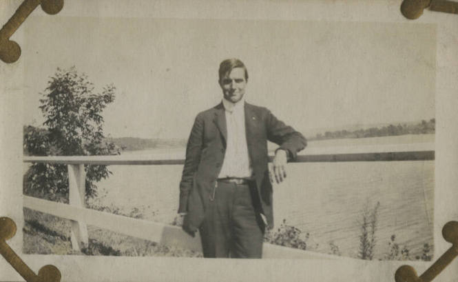 Untitled [Man leans on fence, body of water in background]