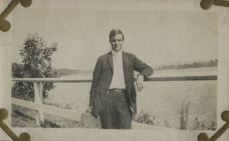 Untitled [Man leans on fence, body of water in background]