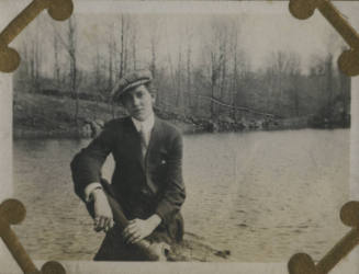 Untitled [Man sits on rock, body of water in background]