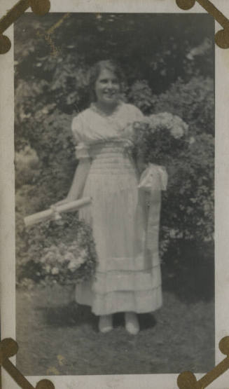 Untitled [Woman stands in garden, holds flowers]