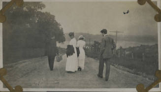 Untitled [Four people walk down dirt road, body of water in the distance]