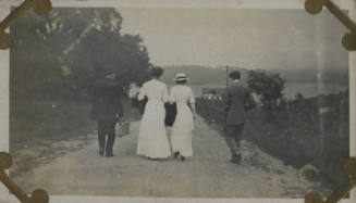 Untitled [Four people walk down dirt road, body of water in the distance]