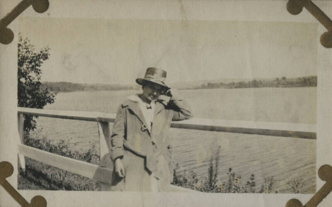Untitled [Woman leans on fence, body of water in background]