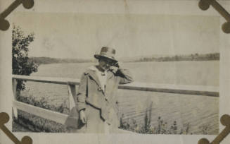 Untitled [Woman leans on fence, body of water in background]