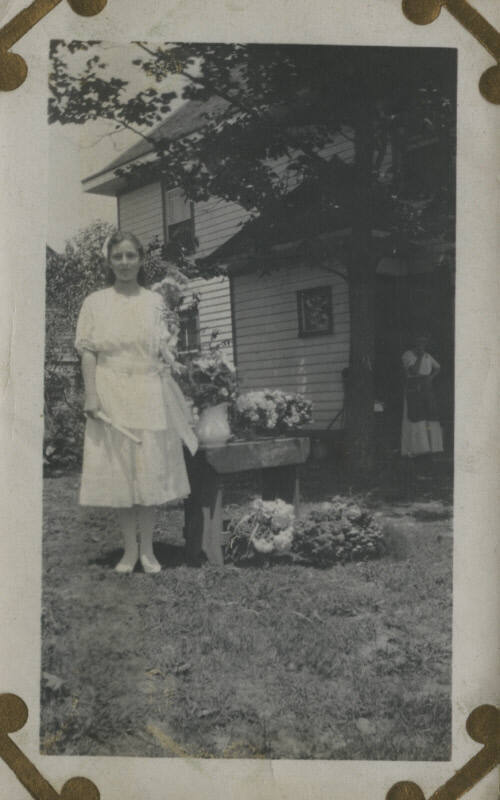 Untitled [Woman stands outside, flowers by her side]