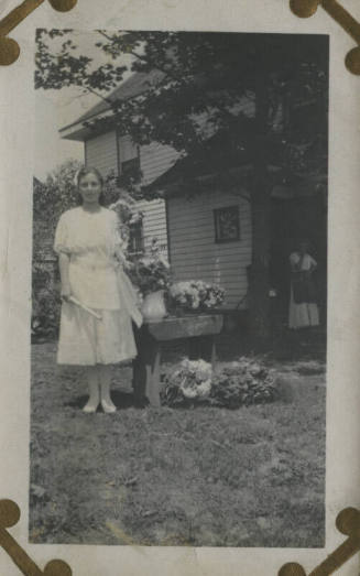 Untitled [Woman stands outside, flowers by her side]
