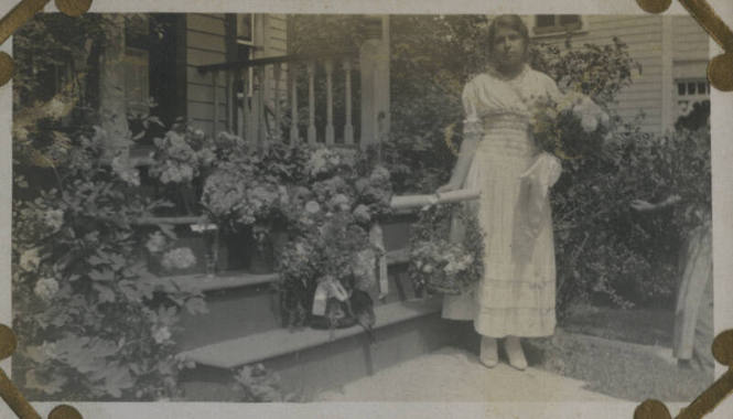 Untitled [Woman stands outside on porch, holds flowers (#1 duplicate)]
