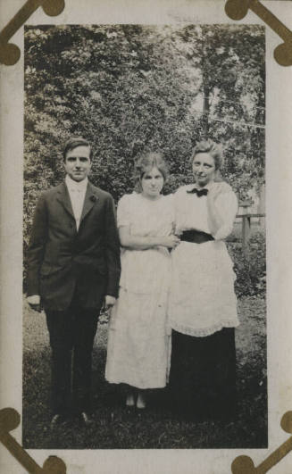Untitled [Two women and a man stand on lawn]