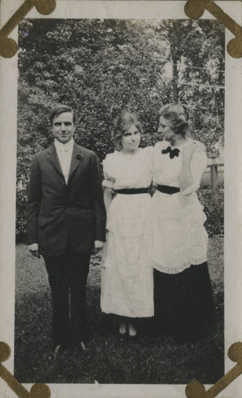 Untitled [Two women and a man stand on lawn]