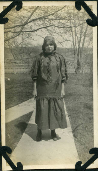 Untitled [Woman stands on concrete path, trees and hills in background]
