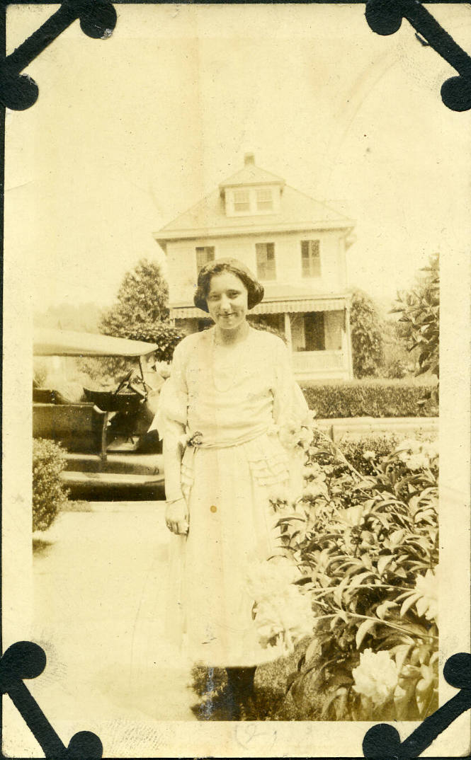 Untitled [Woman stands on front lawn, car and house in background]