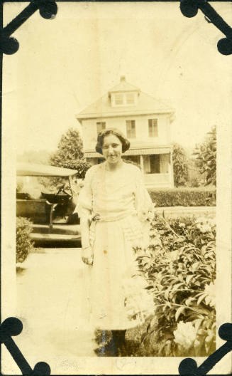 Untitled [Woman stands on front lawn, car and house in background]