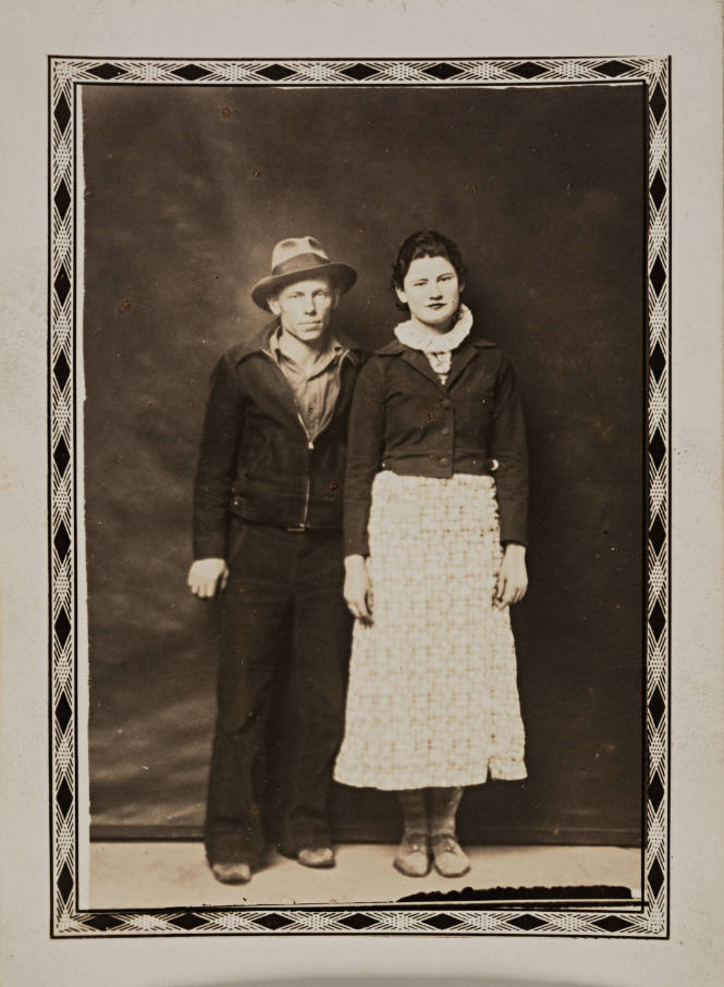 Man in hat, zippered jacket, and woman in sweater, both standing